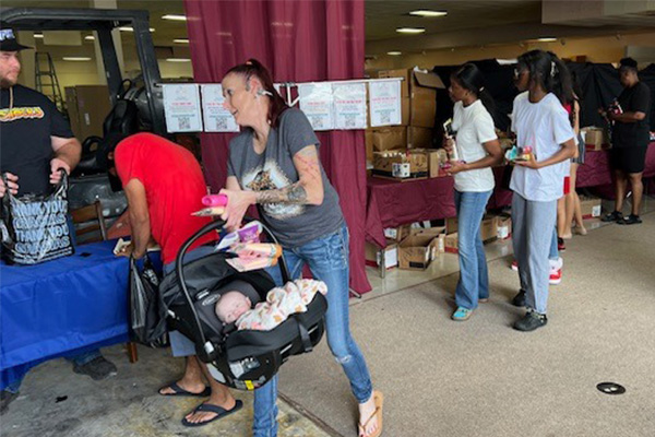 People collecting donated boxes of essential supplies at a Specialized Charities Group distribution event in Florida after a severe storm.