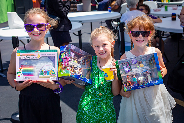 Three children smile while holding new toys they received through Good360 and Toys for Tots, highlighting the impact of toy donations for nonprofits.