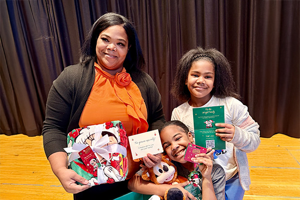 A parent and two children smile while holding Disney gifts and holiday surprises delivered through a Good360 partnership with Disney.