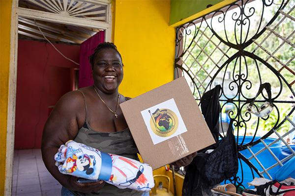 A woman in Jamaica smiles while holding donated relief supplies months after Hurricane Melissa.