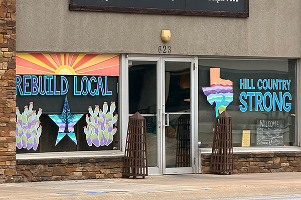 Storefront in Kerrville, Texas, displaying “Rebuild Local” and “Hill Country Strong” window art following historic flooding.