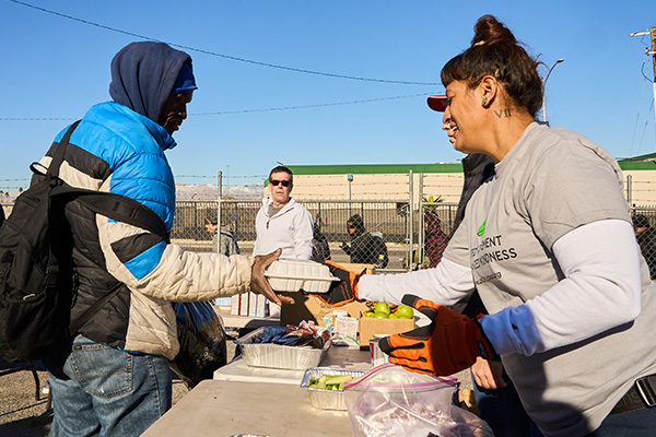 Volunteer hands a meal to an individual during a Las Vegas outreach event providing food, hygiene services, and essential goods.