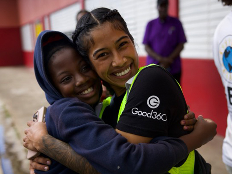Two young women smiling and embracing at a Good360 community event