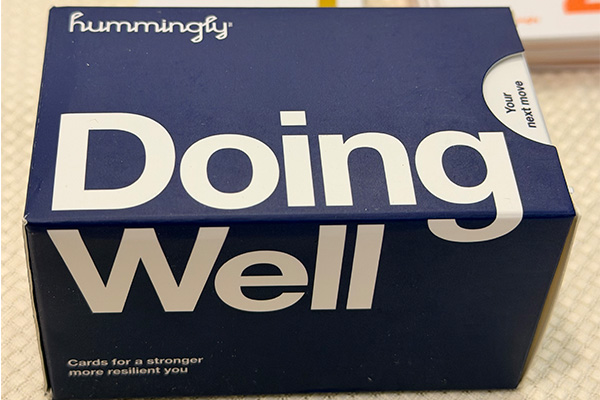 A navy blue box for the Hummingly "Doing Well" card deck, subtitled "Cards for a stronger, more resilient you," with cards fanned out behind it.