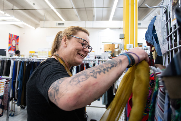 A WellPower staff member smiles while organizing colorful clothing on a rack inside WellPower's Shopette, where clients can choose clothing that fits their size and style.