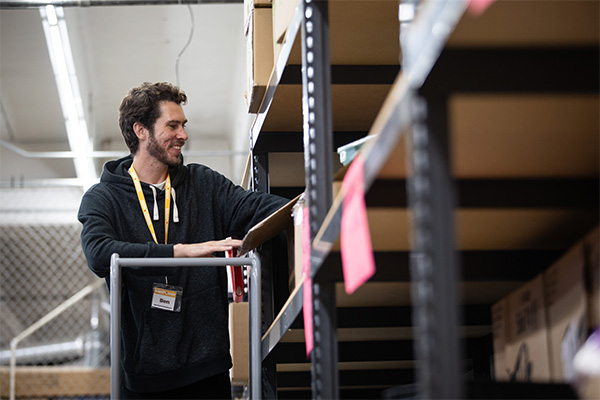 Ben, a WellPower vocational trainee with lived experience of houselessness, smiles while organizing shelves in WellPower's donation warehouse in Denver, Colorado.