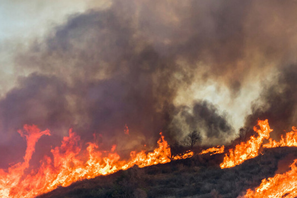 Flames and heavy smoke from a wildfire burn across a hill